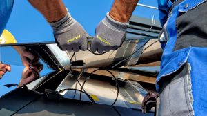 The image shows two people’s legs and hands as they work together to install a solar PV panel into a wall or roof.