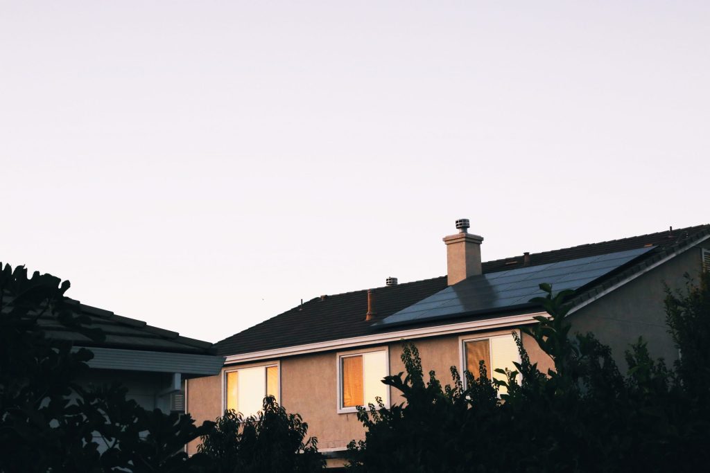 Slightly overcast sunshine reflects on the windows and solar PV panels of a two-storey house.